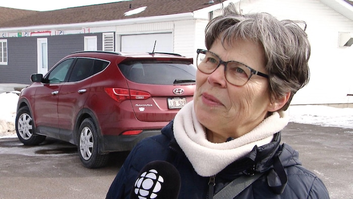 Une femme dans un stationnement, près d'une voiture rouge.