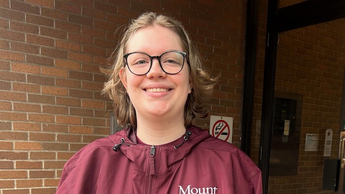Une femme vêtue d'un imperméable aux couleurs de l'Université Mount Allison pose pour une photo dans l'entrée d'un édifice à bureaux.