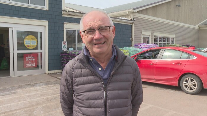 Un homme dans un stationnement devant une porte d'épicerie ouverte.