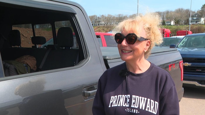 Une femme qui porte des lunettes fumées et un chandail de l'Île-du-Prince-Édouard est debout dehors près d'une camionnette.
