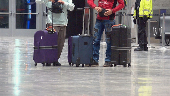 Le bas du corps de deux personnes, avec des valises à leurs pieds.