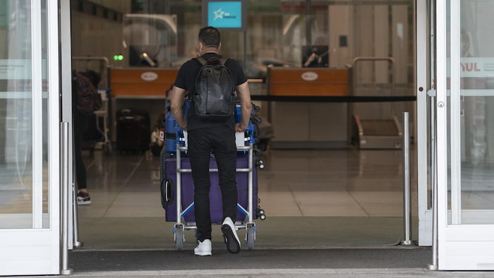 Un voyageur pousse un chariot de valises en entrant à l'aéroport international Pierre-Elliott-Trudeau de Montréal.