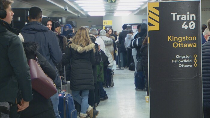 Des voyageurs, de dos, attendent en file.
