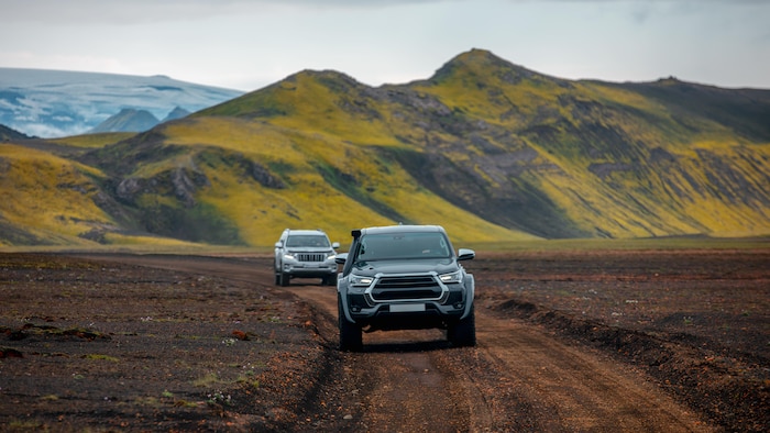 Deux véhicules roulent au pied de montagnes en Islande.