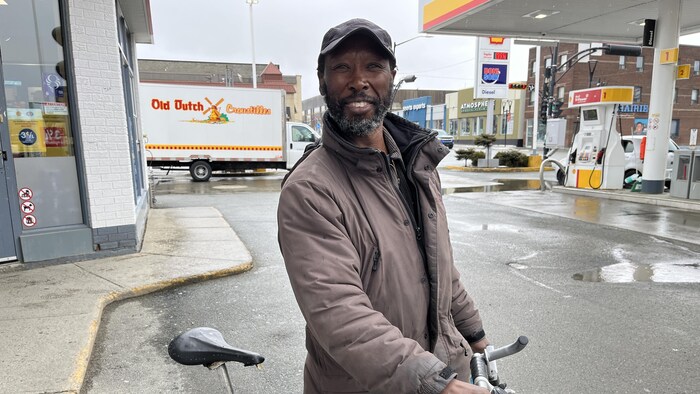Vuyani Gxoyiya tient son vélo dans le stationnement d'une station-service.