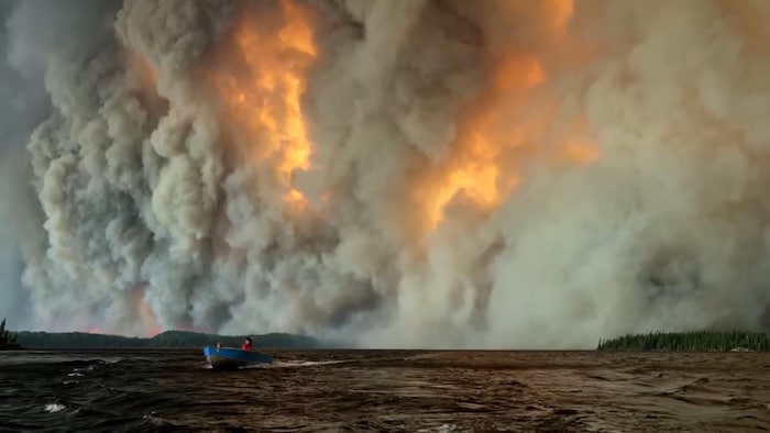 Un bateau s'éloigne d'un immense feu de forêt.