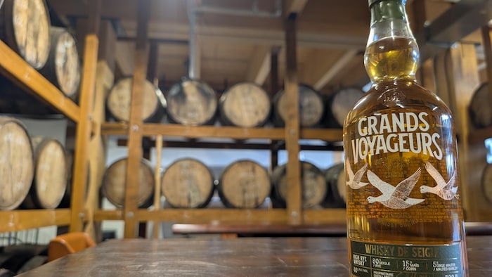 Une bouteille de whisky devant des barils.