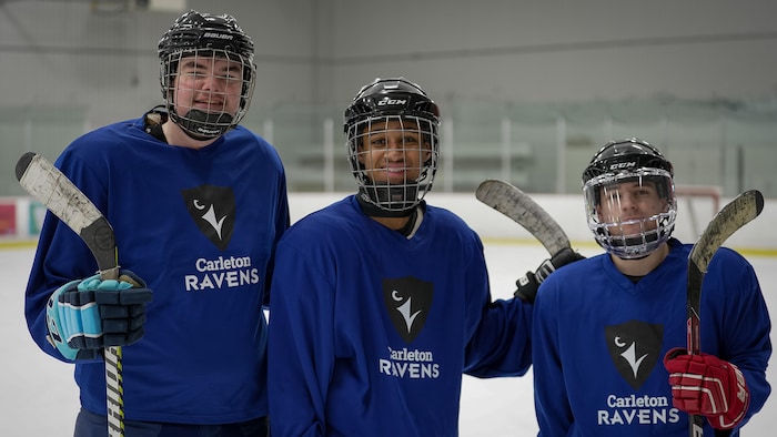Trois hockeyeurs, dont un joueur noir au centre, posent fièrement sur la glace.