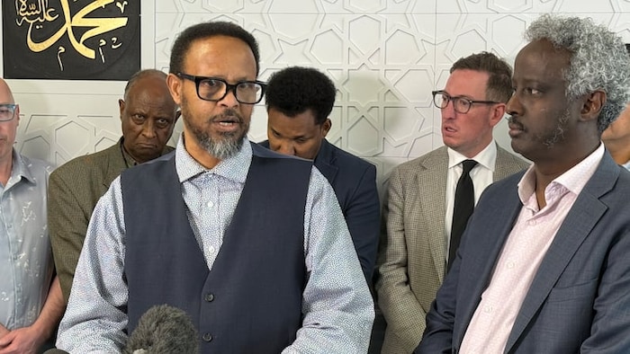 Ali Wahed Noor parle devant des micros, entouré de plusieurs personnes