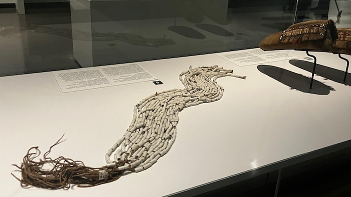 Un objet dans une vitrine de musée est constitué de perles de wampum blanches.