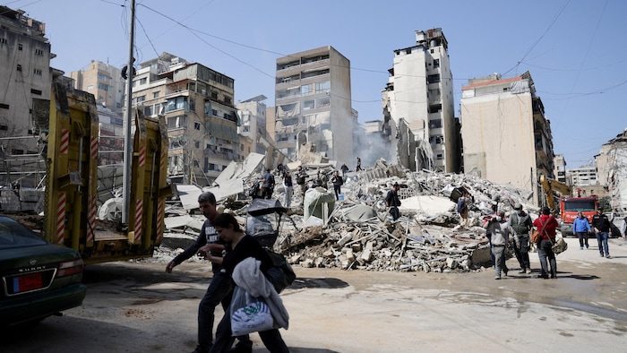 Des gens marchent dans les décombres d'un bâtiment totalement détruit.