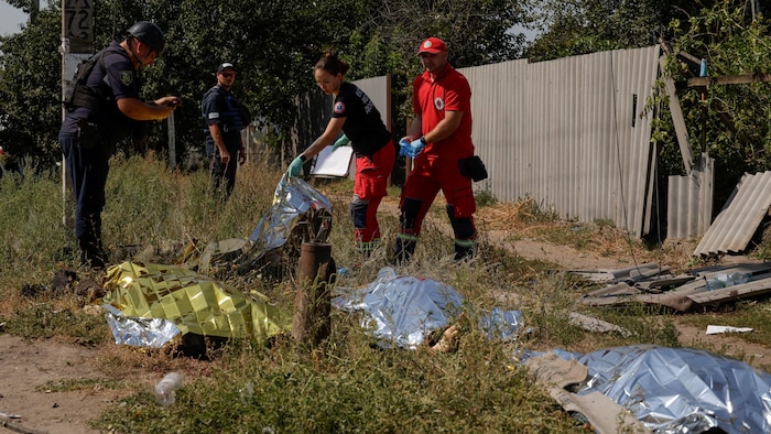 Des ambulanciers et policiers inspectent les corps de victimes, qui sont recouverts par des couvertures de survie.