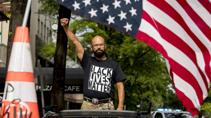 Le nom de George Floyd est écrit sur le pare-brise alors que John Coy porte un t-shirt sur lequel on peut lire « Black Lives Matter » et se tient debout à travers son toit ouvrant, le poing en l'air, 16e rue nord-ouest, rebaptisée « Black Lives Matter Plaza » près de la Maison-Blanche, le vendredi 19 juin, à Washington.