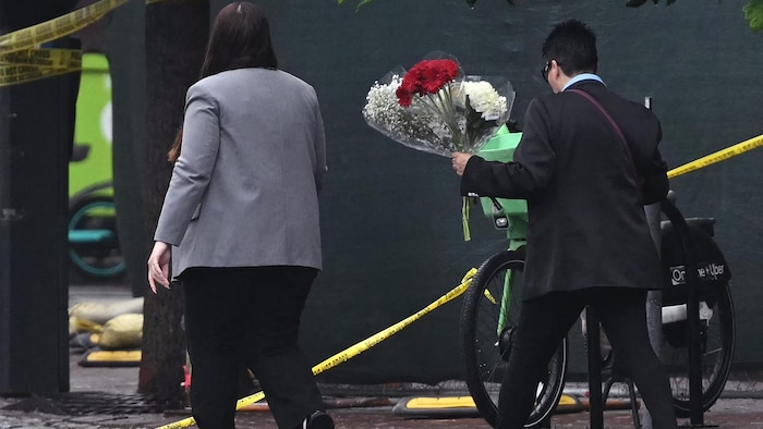 Deux personnes, dont l'une tenant un bouquet de fleurs, marchent à l'extérieur d'un périmètre de sécurité. 