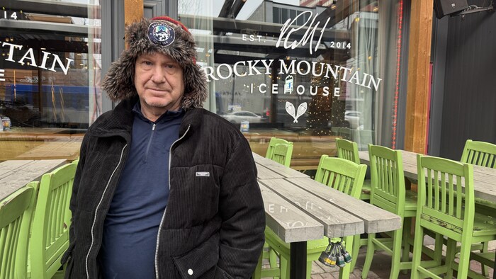 Un homme avec une tuque devant des tables et des chaises dehors.