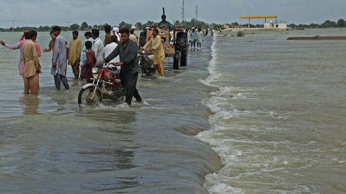 Des personnes traversent à pied un vaste terrain inondé, le 25 août 2022. 