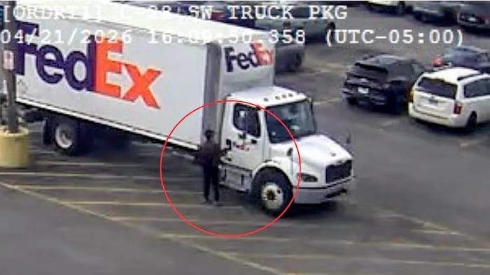 Un homme portant des vêtements sombres se tient près d’un camion FedEx blanc.