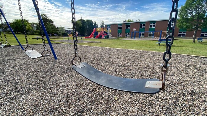 Des balançoires d'un terrain de jeu avec une école en arrière-plan.