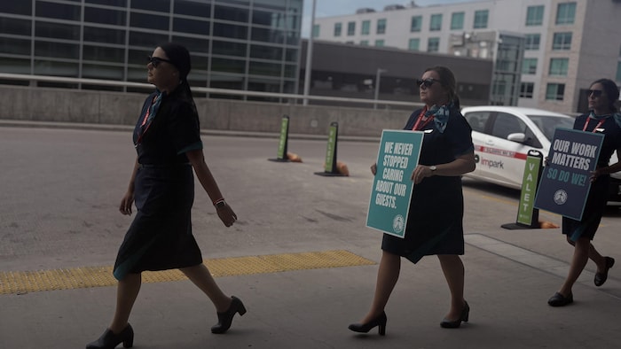 Trois membres du personnel de WestJet portant des pancartes réclamant de meilleures conditions de travail.