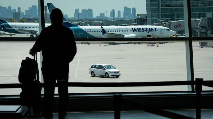 Un passager avec sa valise regardant par la fenêtre du terminal un avion de WestJet.