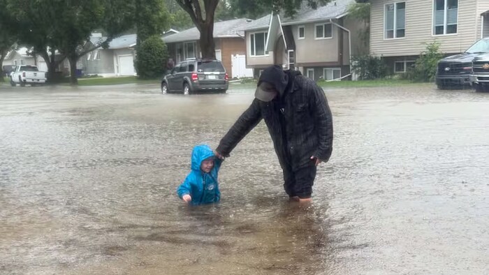 Un enfant et un adulte debout dans une rue inondée.