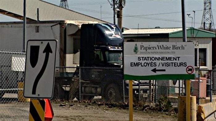 Un panneau qui signale l'entrée de l'usine, avec un camion en arrière-plan.