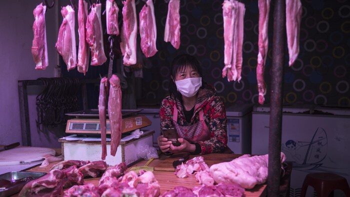 Une femme consulte son téléphone cellulaire au milieu de pièces de viande suspendues à des crochets. 