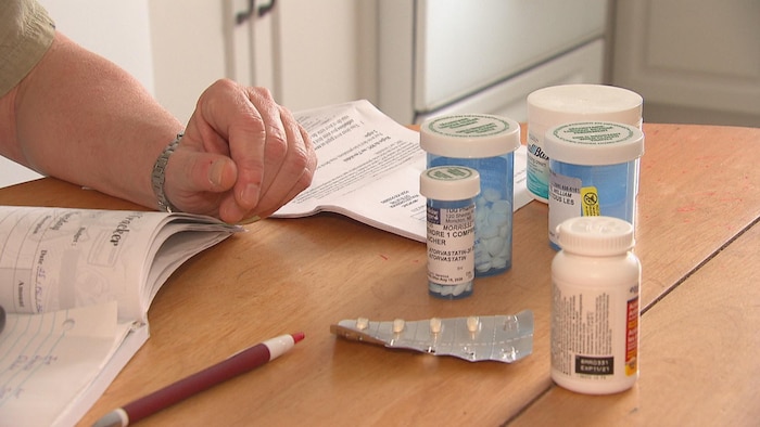 Gros plan sur les mains d'un homme qui tient un livret sur une table avec des médicaments.