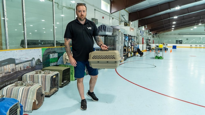 William Woodstock qui tient une cage de transport pour animaux, étant debout dans l'enceinte de l'aréna Grandview.