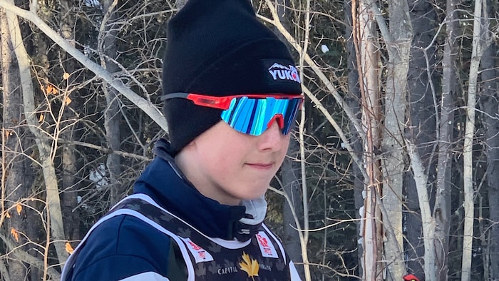 Un jeune athlète pose en tenue de ski de fond devant des arbres en hiver.
