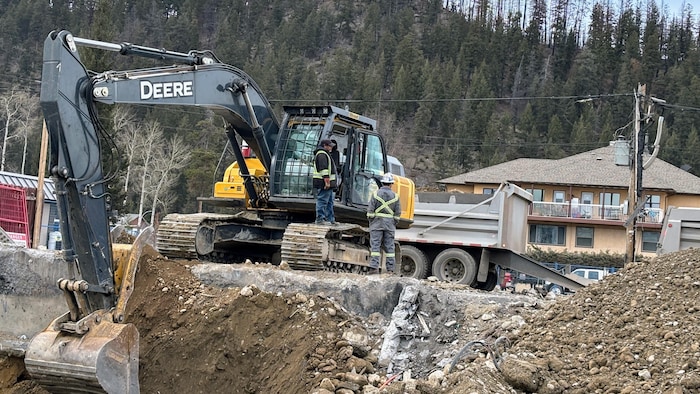 Un homme fait fonctionner une pelle mécanique devant un trou. 