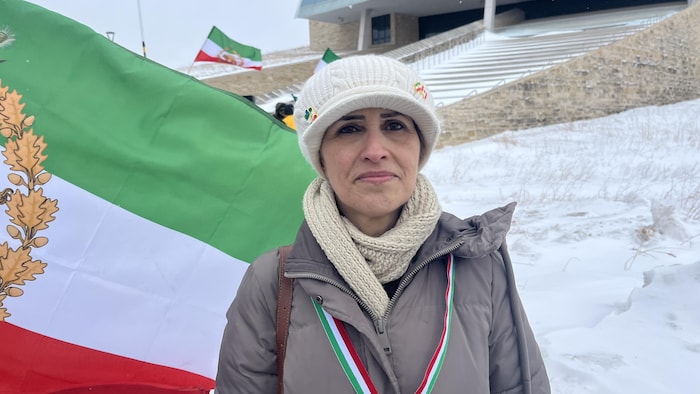 Shahla Shojaei devant un grand drapeau iranien dans un décor enneigé.