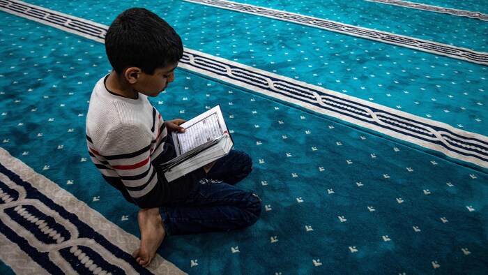 Un enfant lit le coran sur un tapis de prière.
