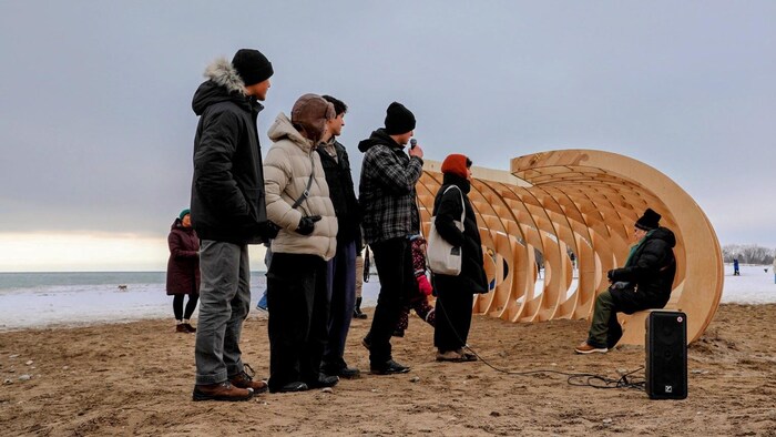 Une personne ainée assit dans l’installation « Crest » représentant une vague en bois sur la place du lac Ontario à Toronto le 16 février 2026.