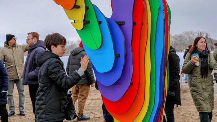 Un jeune garçon compare sa main avec l’installation « Embrace » représentant deux mains multicolores se refermant sur la chaise de sauveteur de la plage du lac Ontario, à Toronto, le 16 février 2026.