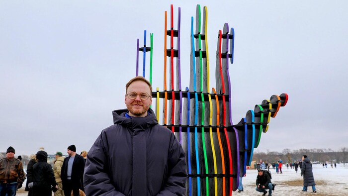 Will Cuthbert devant une partie de son installation « Embrace » représentant l’une de deux mains faites de fines lamelles de couleurs vives sortant du sable gelé pour saisir l’horizon.
