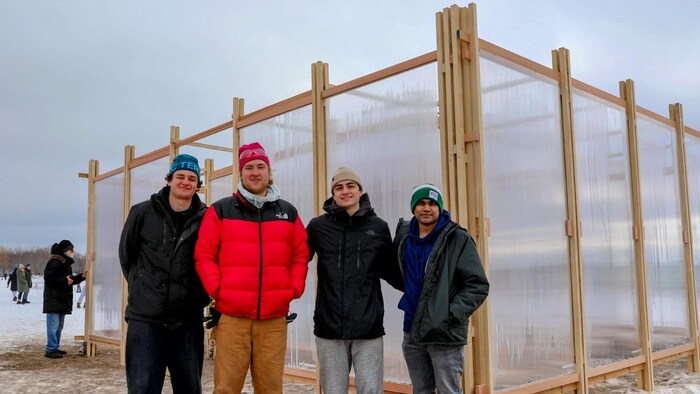L’équipe de conception de l’œuvre « Glaciate » devant son installation composée d’une série de panneaux verticaux en polycarbonate, remplis d’eau du lac voisin, crée des lentilles de glace qui glacent le poste. Au gré des cycles de gel et de dégel, les panneaux alternent entre transparence, translucidité et opacité totale.