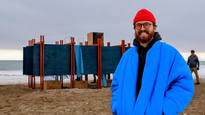 Andrew Clark devant son installation « Specularia » soit cinq ouvertures encadrées, face au lac, offrant l’aperçu d’un mélange de réalité et d’illusion. À travers des miroirs semblables à des périscopes, disposés à 45 degrés, ceux qui les traversent perçoivent le sol, le ciel, la promenade et leur propre image avant de découvrir enfin la véritable image qui se dessine.