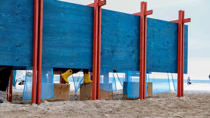 Un enfant traversant l’installation « specularia », cinq ouvertures encadrées, face au lac, offrent un aperçu d’un mélange de réalité et d’illusion, alors qu’on ne voit que ses bottes jaunes sur la plage du lac Ontario à Toronto le 16 février 2026.