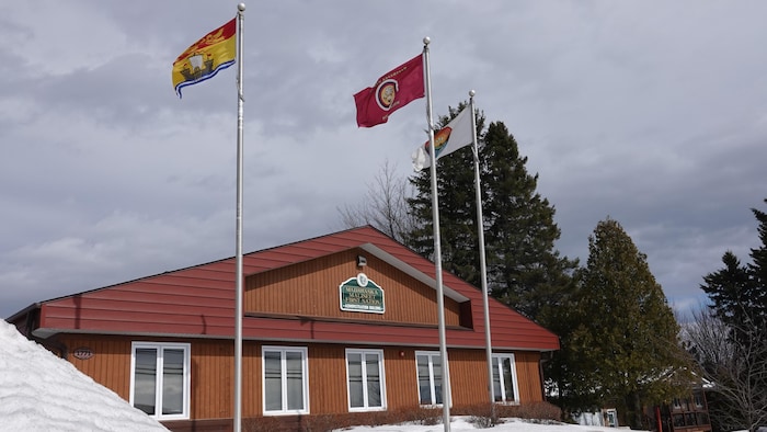 Trois drapeaux flottent devant une bâtisse.