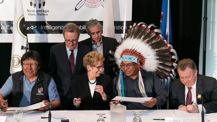 La première ministre, deux représentants autochtones, et quelques ministres signent un accord à une table.