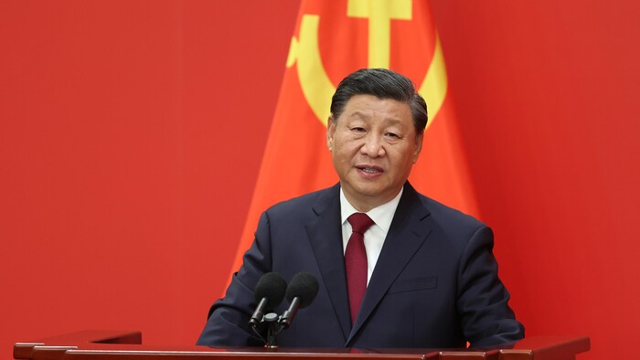الرئيس الصيني شي جين بينغ يلقي خطاباً، أمامه ميكروفون وخلفه علم الحزب الشيوعي الصيني.