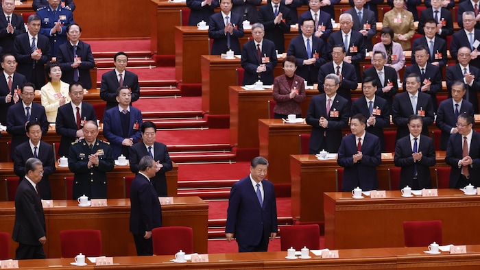 Le président chinois est applaudi par des dizaines de personnes qui sont debout derrière des rangées de bureaux.