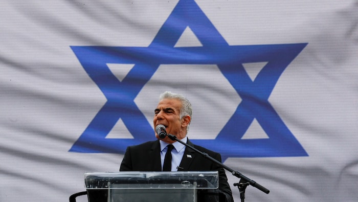 M. Lapid parle devant une écran géant montrant un drapeau israélien.