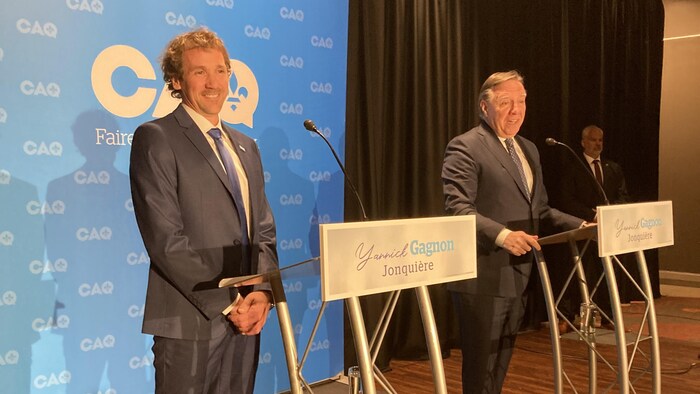 Yannick Gagnon et François Legault sur une scène. Le loge de la CAQ en arrière-plan.