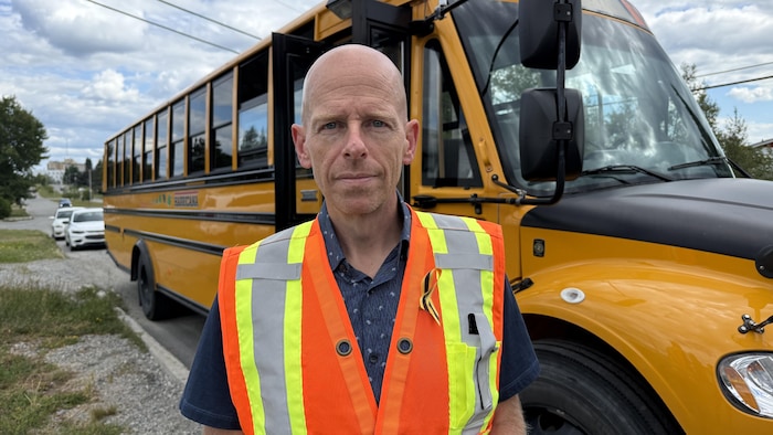 Un homme debout devant un autobus scolaire pour la photo.  
