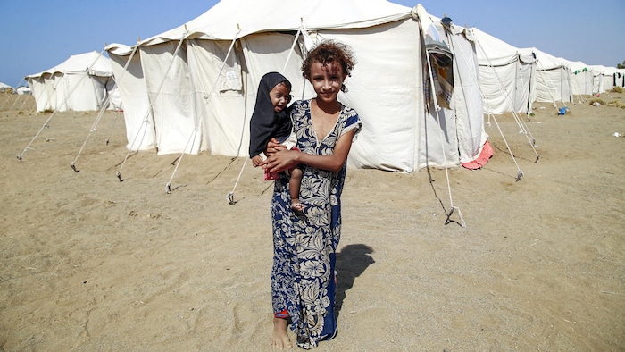 Un fillette portant un bébé dans un camp situé dans le désert.