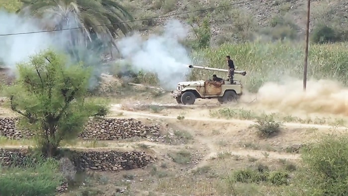 Image d'un véhicule de guerre doté d'un lance-missile, dans un paysage aride ponctué de palmiers.