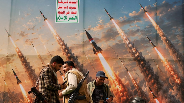 Des militants houthis se tiennent sur une estrade devant une bannière représentant des missiles houthis.