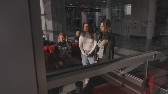 Kim Bouchard-Chayer et Annie-Claude Pelletier, filmée à travers une fenêtre, en train de discuter avec une jeune femme.